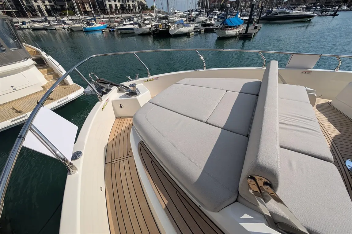 Modern yacht deck featuring a large cushioned seat and a view of boats docked in the marina under clear skies.